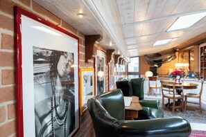 L’intérieur d’un restaurant présente des murs en briques, des tableaux encadrés, des fauteuils en cuir et un espace repas avec des tables et des chaises.
