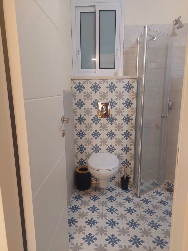 A bathroom with a toilet, a shower, and a patterned tile floor.