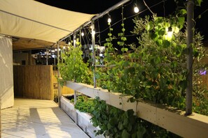 A rooftop garden with plants, a wooden deck, and string lights.