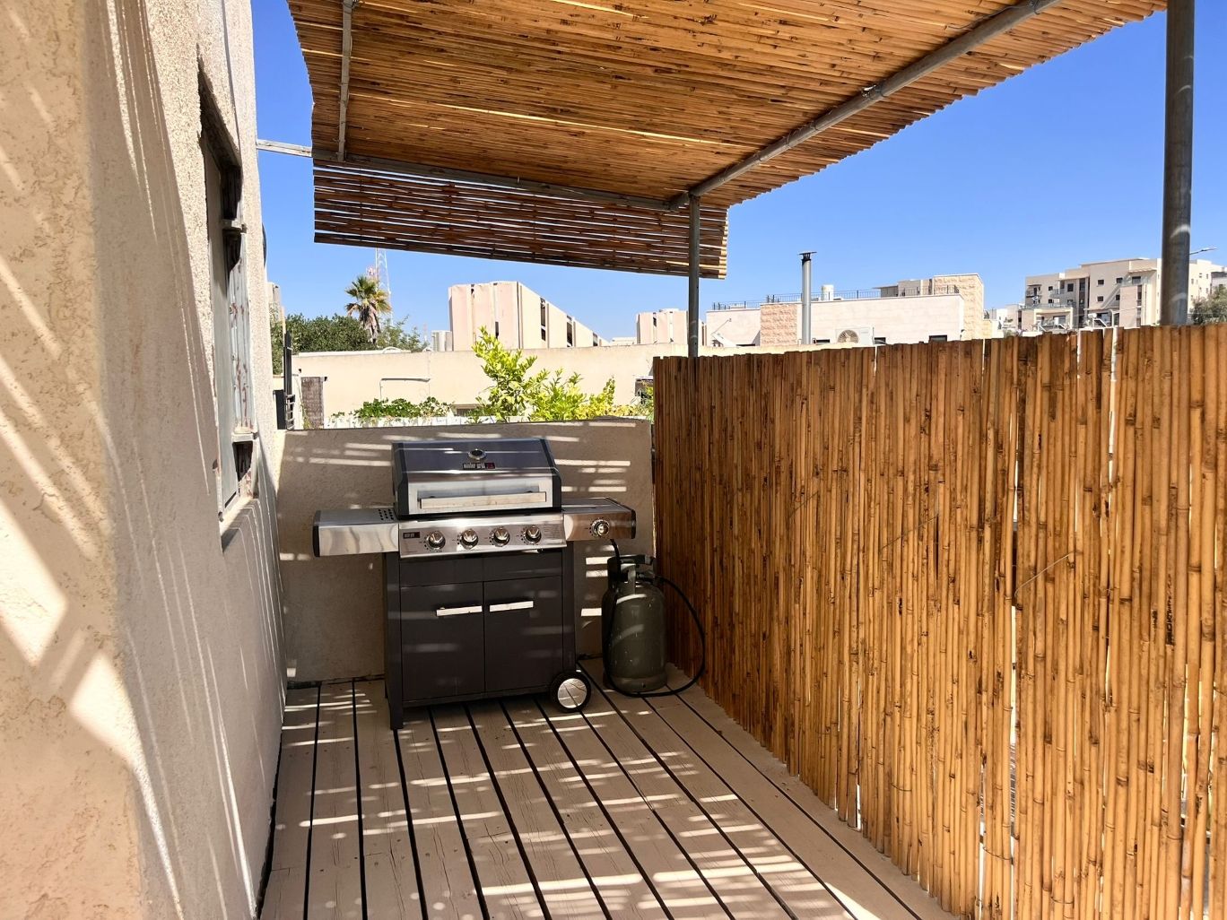 Zona de barbacoa al aire libre con parrilla y basurero, delimitada por una valla de madera y un pérgola.