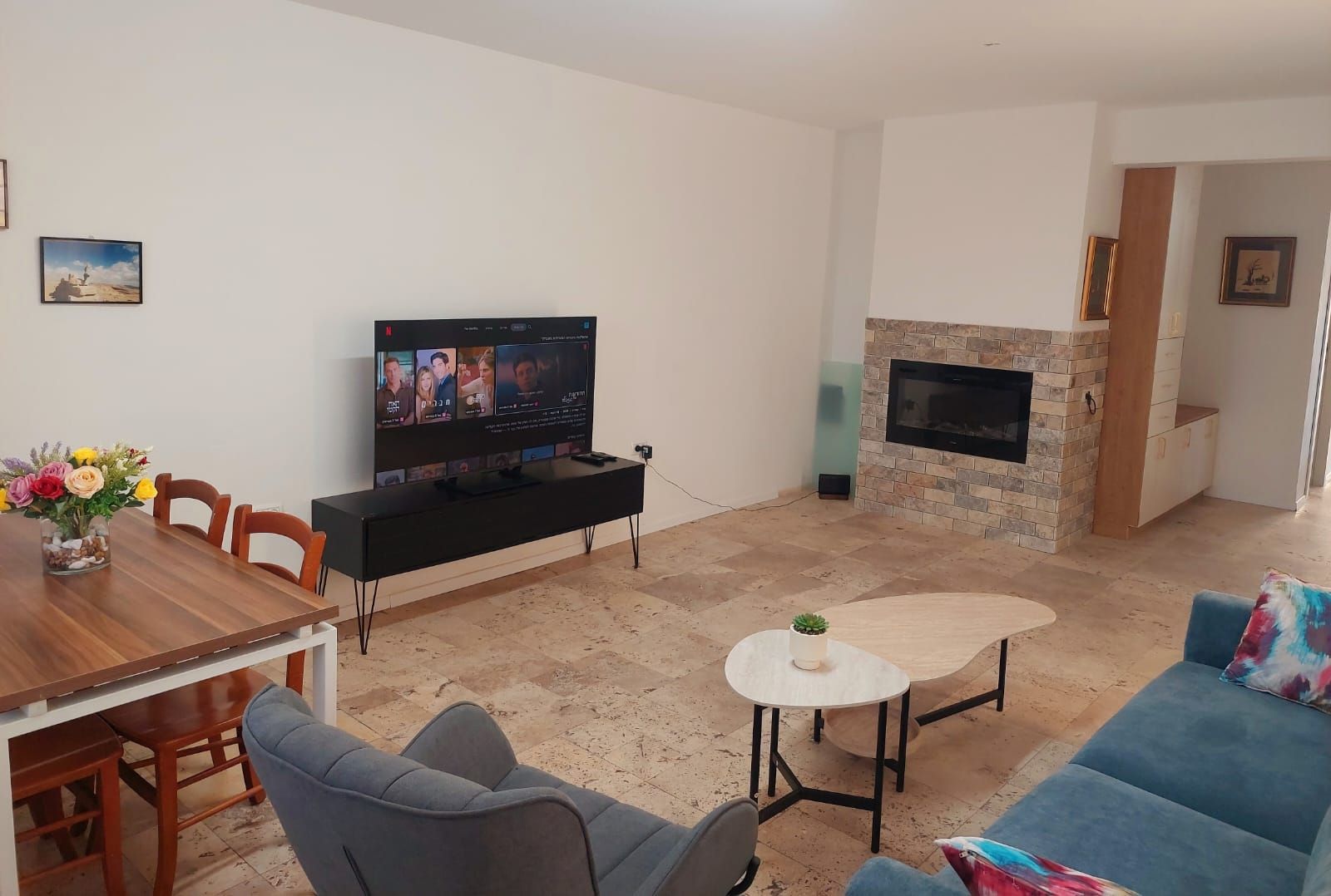 Una sala de estar con televisor de pantalla plana, una mesa de comedor con sillas, un sofá, una pequeña mesa de centro y una chimenea.