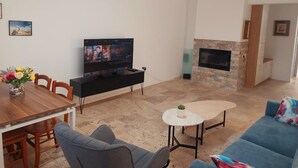 Una sala de estar con televisor de pantalla plana, una mesa de comedor con sillas, un sofá, una pequeña mesa de centro y una chimenea.