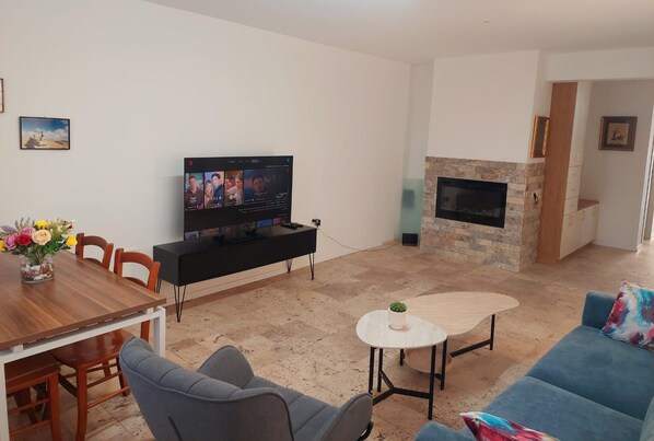 A living room with a flat-screen TV, a dining table with chairs, a sofa, a small coffee table, and a fireplace.
