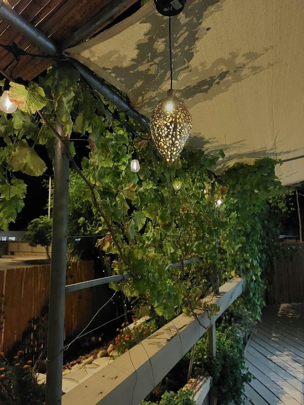 Ein überdachter Außenbereich mit einer Pergola, Kletterpflanzen und hängenden Lichterketten.