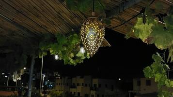 An outdoor seating area with a bench and a stone planter, under a wooden pergola with a hanging light fixture.