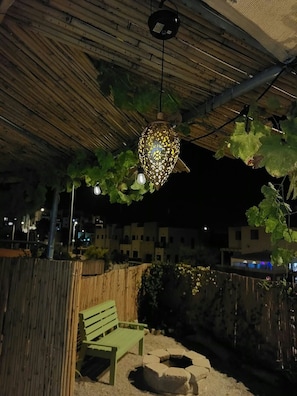 An outdoor seating area with a bench and a stone planter, under a wooden pergola with a hanging light fixture.