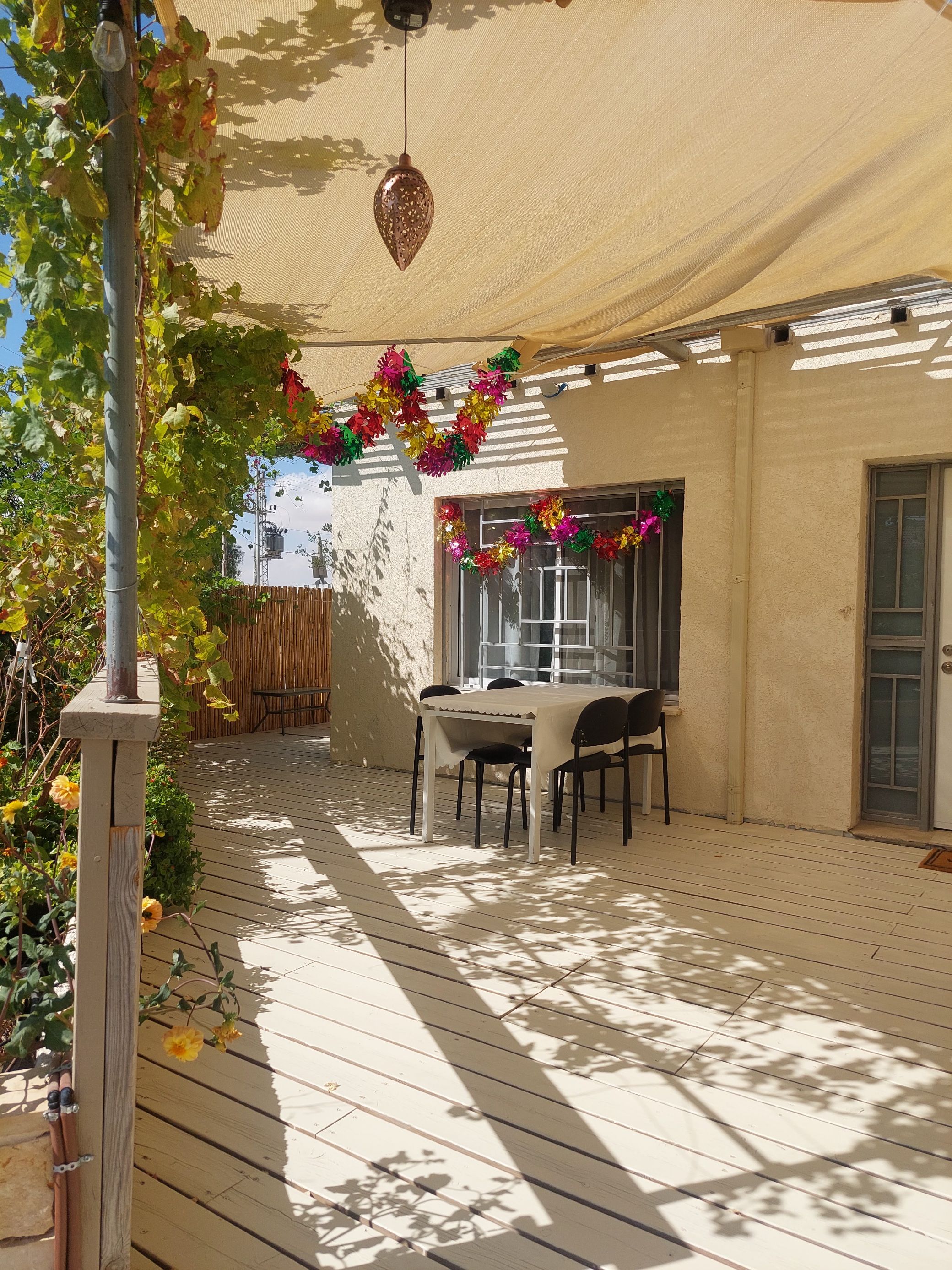 Een overdekt terras met een tafel en stoelen, omgeven door een pergola met klimplanten.