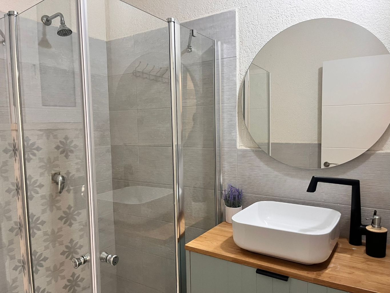 A modern bathroom with a glass-enclosed shower, a white sink, and a round mirror.