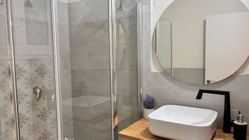 A modern bathroom with a glass-enclosed shower, a white sink, and a round mirror.