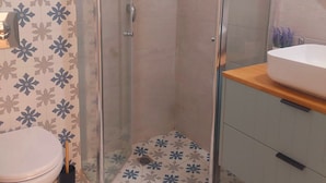 Un baño con ducha de vidrio, inodoro y lavamanos con espejo.