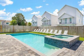 A swimming pool with lounge chairs, a wooden fence, and a row of white houses in the background. - Ocean Breeze: Heated Pool & Hot Tub, Free Golf Cart, Two Arcade Rooms (Miramar Beach)