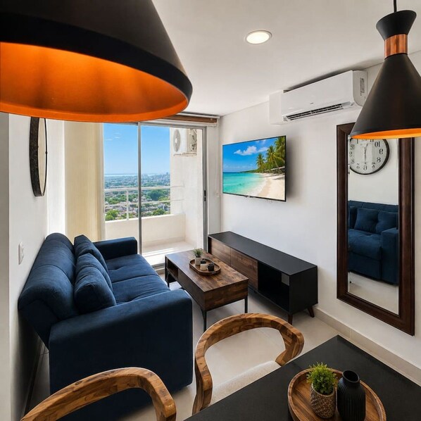 A modern living room with a sofa, a coffee table, and a TV. There is a large window with a view of the city. - Tropical Midnight | Sunset Views & Pool, Wi-Fi (Cartagena)