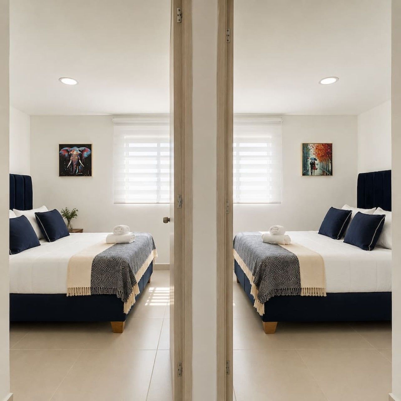 A mirrored view of a hotel room with two beds, a window with blinds, and artwork on the walls.