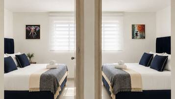 A mirrored view of a hotel room with two beds, a window with blinds, and artwork on the walls.