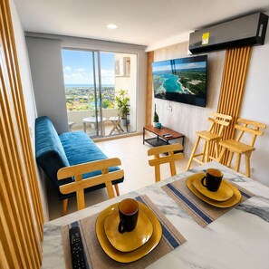 Ein modernes Wohnzimmer mit Sofa, Esstisch, Stühlen, Fernseher und einem Balkon mit Blick.
