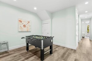 A room with a foosball table, a painting on the wall, and a door leading to another room. - Shellbelle: Steps to Beach, Heated Pool & Hot Spa, Free Golf Cart, 3 Game Rooms (Miramar Beach)