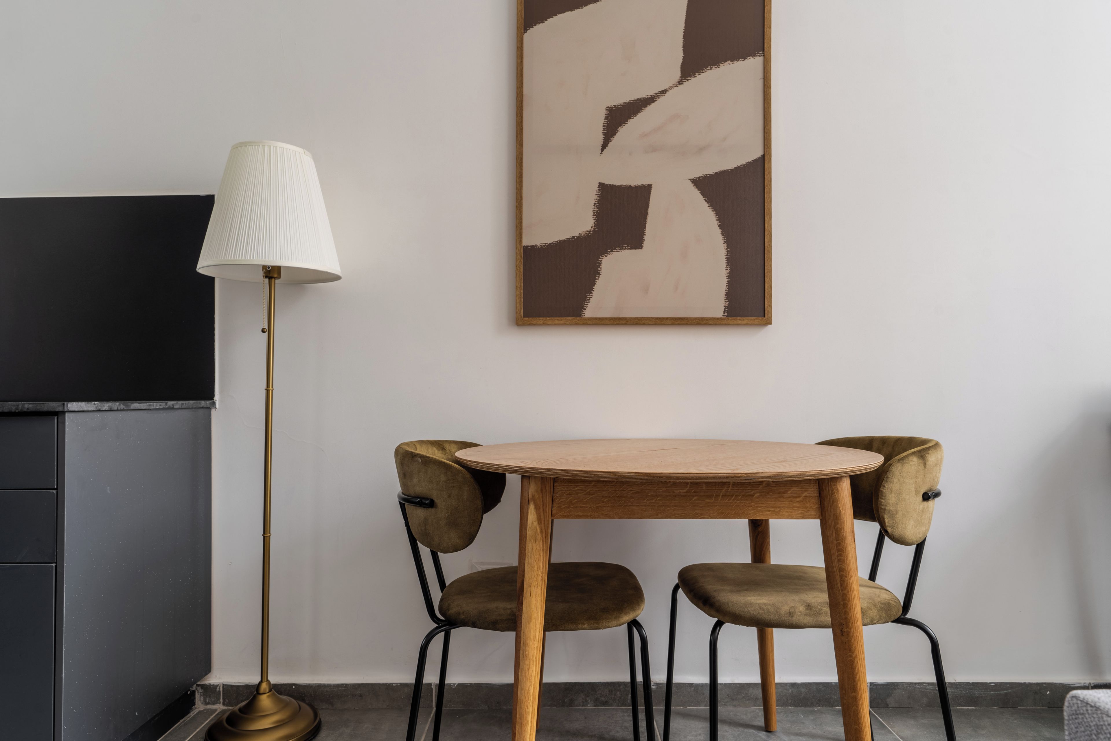 Quarto com mesa de madeira e duas cadeiras, luminária de chão e um quadro na parede.
