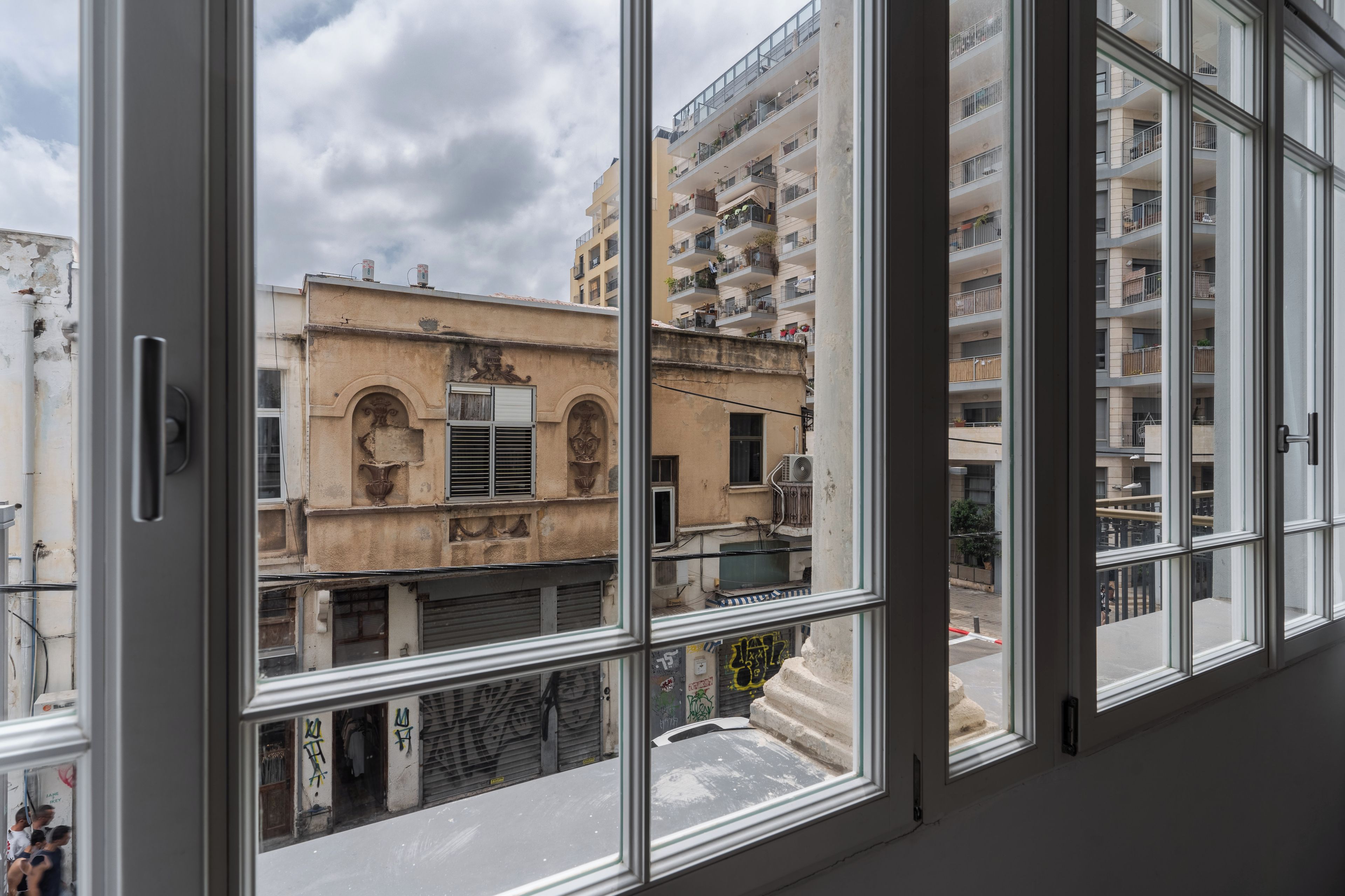 Vista a través de una ventana de un edificio con varios balcones y una calle abajo.