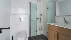 A bathroom with a toilet, a glass shower enclosure, a sink with a mirror, and a wooden cabinet. - Blueground - Historical Preserved Estate (Tel Aviv-Yafo)