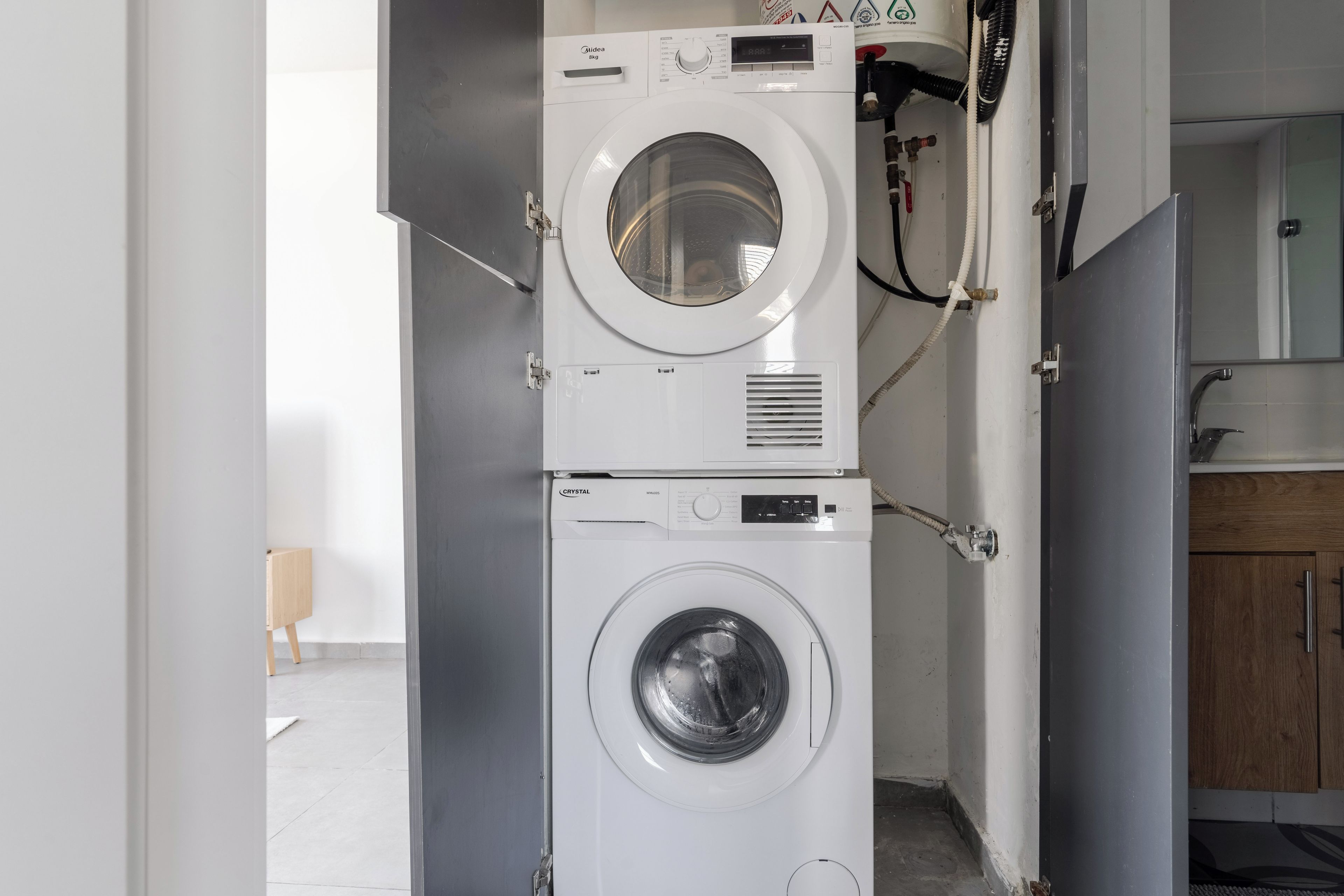 Un espacio de lavandería compacto con dos lavadoras apiladas, un mueble pequeño y una puerta de madera.