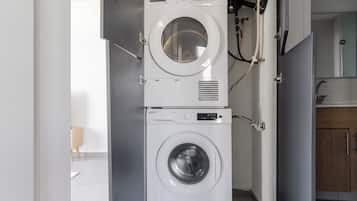 Un espacio de lavandería compacto con dos lavadoras apiladas, un mueble pequeño y una puerta de madera.