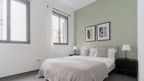 A bedroom with a bed, two bedside tables, a window, and two wall-mounted artworks. - Blueground - Historical Preserved Estate (Tel Aviv-Yafo)