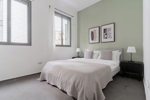 A bedroom with a bed, two bedside tables, a window, and two wall-mounted artworks. - Blueground - Historical Preserved Estate (Tel Aviv-Yafo)