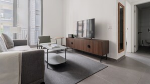A modern living room with a sofa, coffee table, TV, and a cabinet. - Blueground - Historical Preserved Estate (Tel Aviv-Yafo)