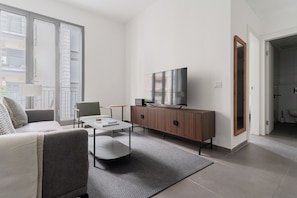 A modern living room with a sofa, coffee table, TV, and a cabinet. - Blueground - Historical Preserved Estate (Tel Aviv-Yafo)