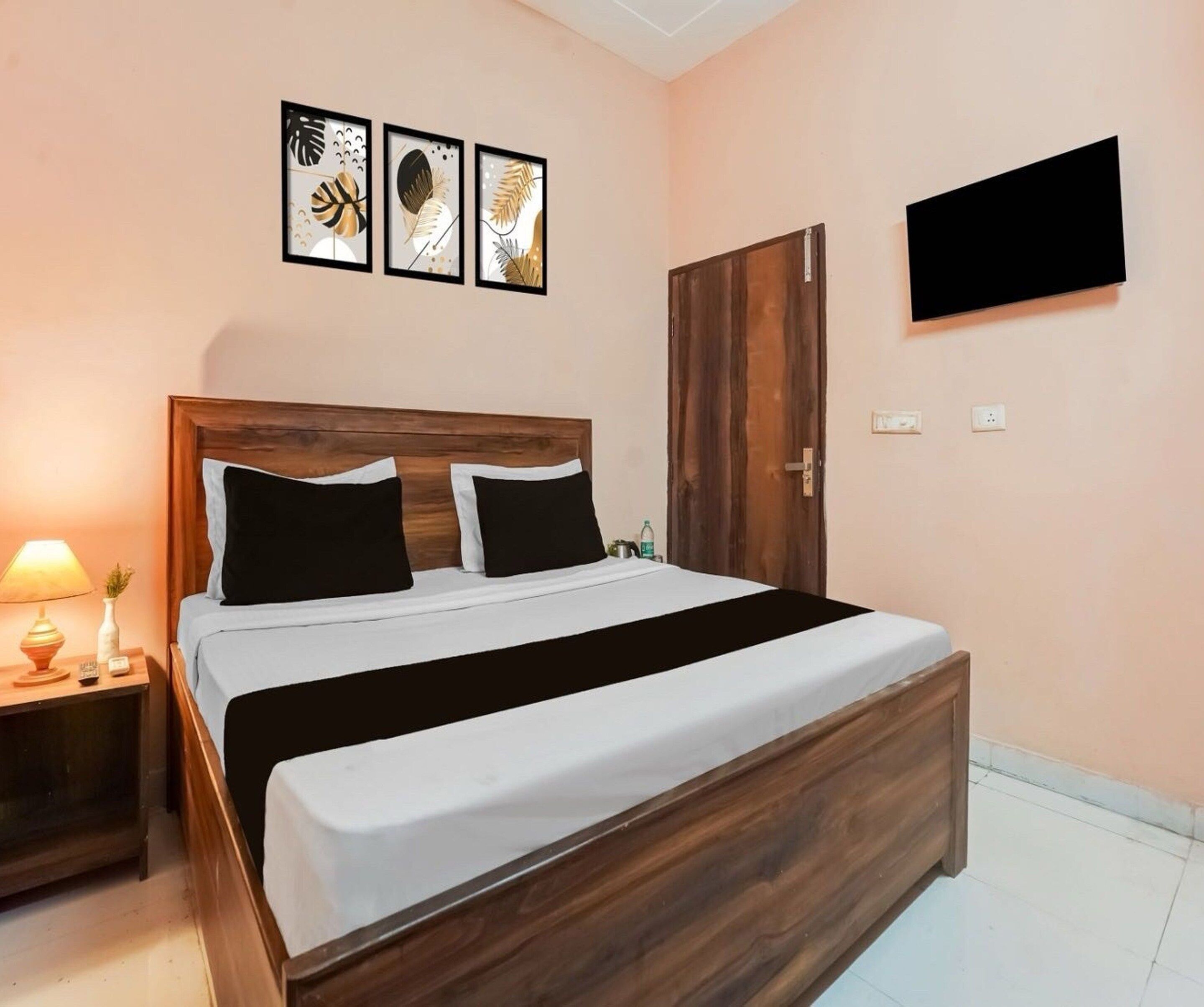 Una cama bien hecha con cabecera de madera, una mesita de noche con lámpara y un televisor fijado a la pared.