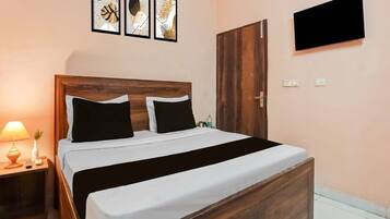 Una cama bien hecha con cabecera de madera, una mesita de noche con lámpara y un televisor fijado a la pared.