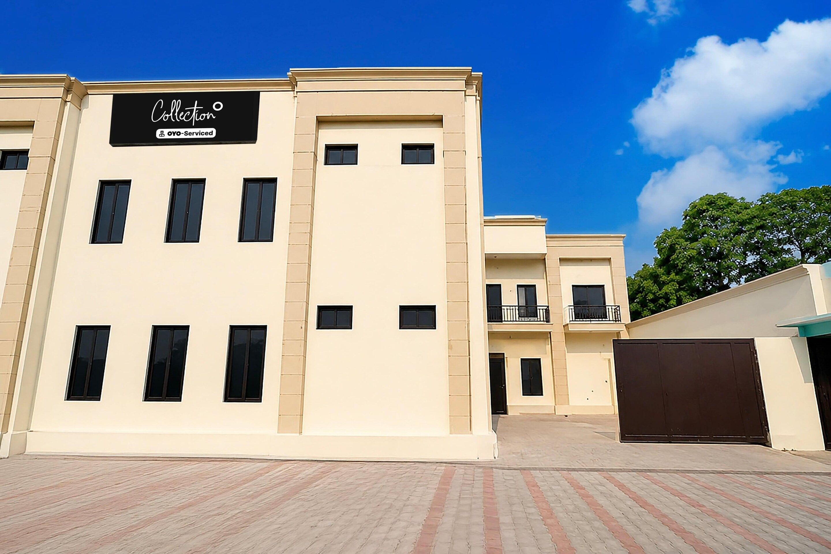 A multi-story building with a beige facade, a sign reading 'Collection OYO-Serviced', and a gated entrance.