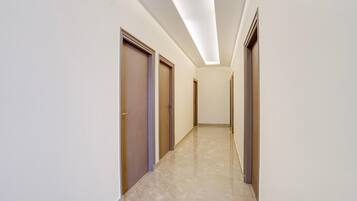 A corridor with doors on both sides, a tiled floor, and a ceiling with recessed lighting.