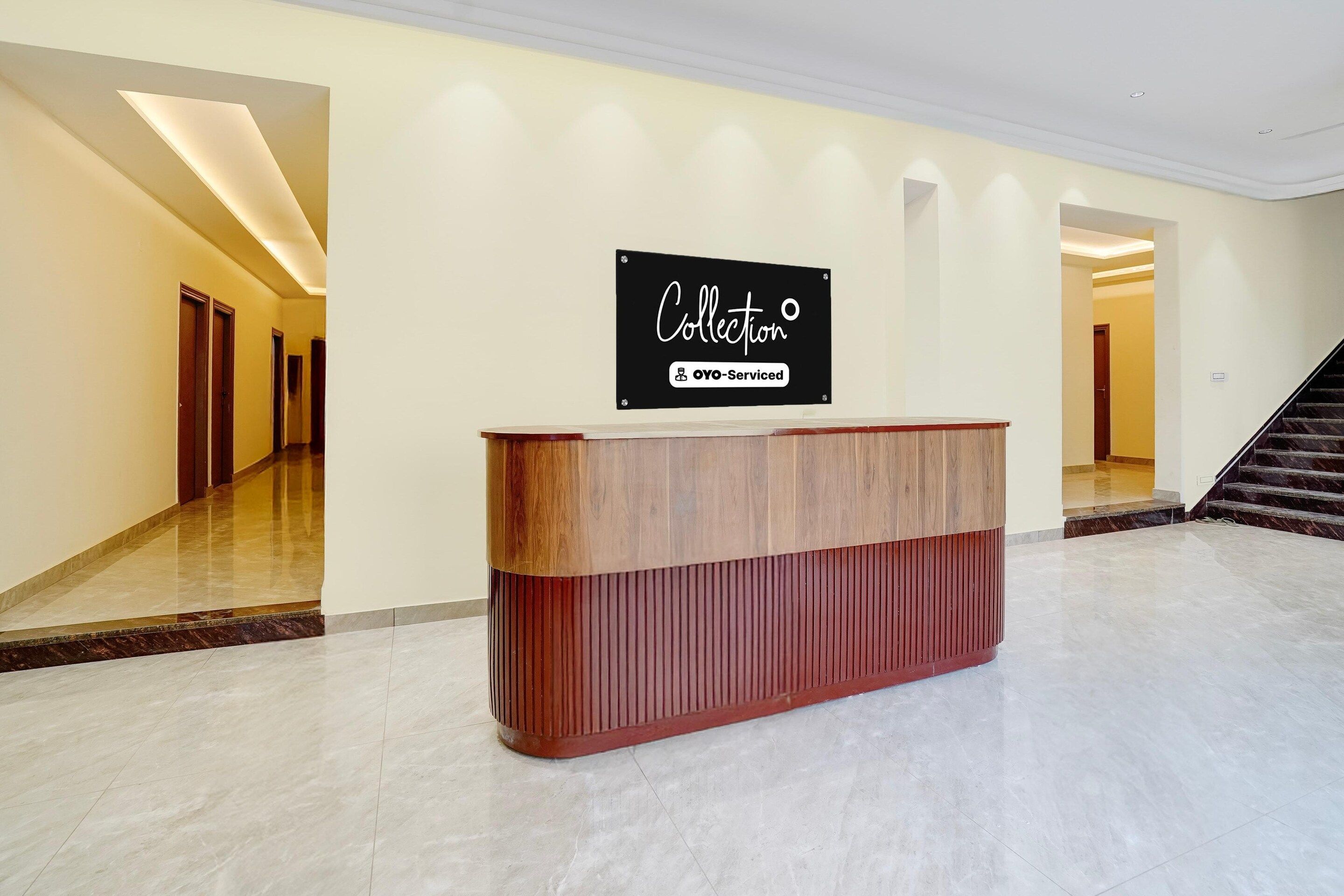 A reception desk with a sign above it, a staircase to the right, and a hallway with doors on the left.