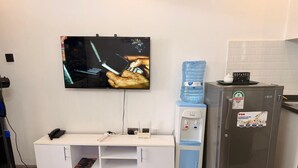 Een kitchenette met een koelkast, een waterdispenser, een flatscreen-tv, een bureau met telefoon en een wandgemonteerd kabelmanagement systeem.