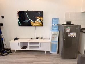 Una kitchenette con refrigerador, dispensador de agua, televisión de pantalla plana, escritorio con teléfono y sistema de organización de cables en la pared.