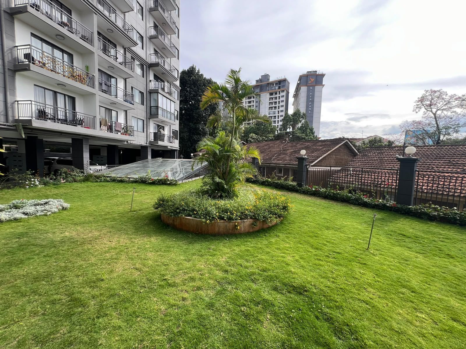 Un patio con un jardín central, un edificio de varios pisos con balcones y una cerca que rodea el área.