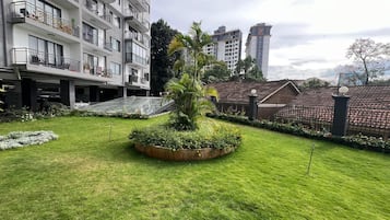Ein Innenhof mit einem zentralen Garten, ein mehrstöckiges Gebäude mit Balkonen und ein Zaun, der das Areal umgibt.