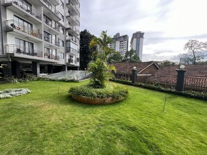 Un patio con un jardín central, un edificio de varios pisos con balcones y una cerca que rodea el área.
