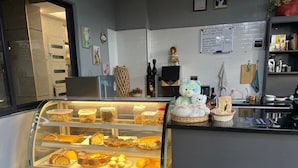 Una vitrina de panadería con diversos productos horneados, una máquina de café y una figura decorativa de un oso.