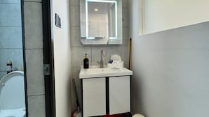 Un baño pequeño con lavamanos, espejo y retrete blancos.