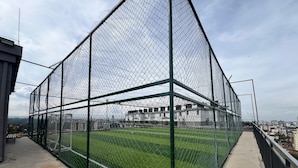 Un campo deportivo rodeado por una cerca de alambre con un sendero de concreto y un banco.