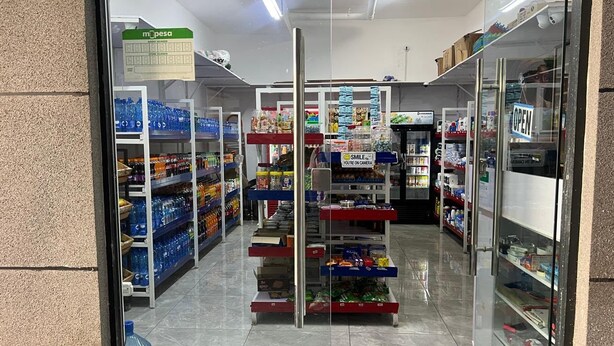 Een winkelinterieur met schappen vol diverse producten, een bordje met 'OPEN' en een bord dat 'U wordt gefilmd' aangeeft.