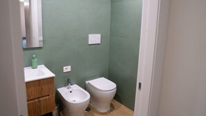 Ein Badezimmer mit Holzboden, einem weißen Waschbecken, einem Bidet und einer Toilette.