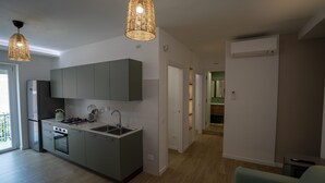 Eine moderne Küche mit grauen Schränken, einem eingebauten Backofen und einer Spüle aus Edelstahl. Zwei Pendelleuchten hängen über der Arbeitsplatte.