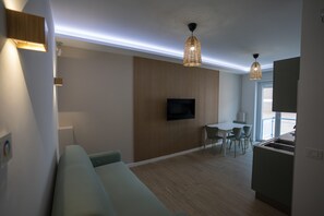 A modern living room with a sofa, a dining area with chairs, a TV mounted on the wall, and a kitchen area with a sink. - Brezza di Mare - Sea, Passion, Relax (Terracina)