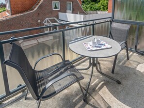A balcony with a table and chairs, a glass railing, and a view of a brick building. - Holiday Apartment With 1 Bedroom (Esens)