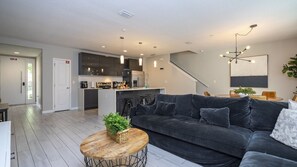 A modern living room with a dark grey sofa, a round wooden coffee table, and a staircase leading to an upper level. - Prime Location 4BR Le Reve with Pool Near Disney (Kissimmee)