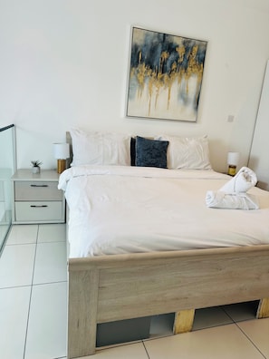 A hotel room with a large bed, two bedside tables, a nightstand, a small potted plant, a painting on the wall, and a towel on the bed. - Phil's Properties At Embassy Gardens GH (Accra)