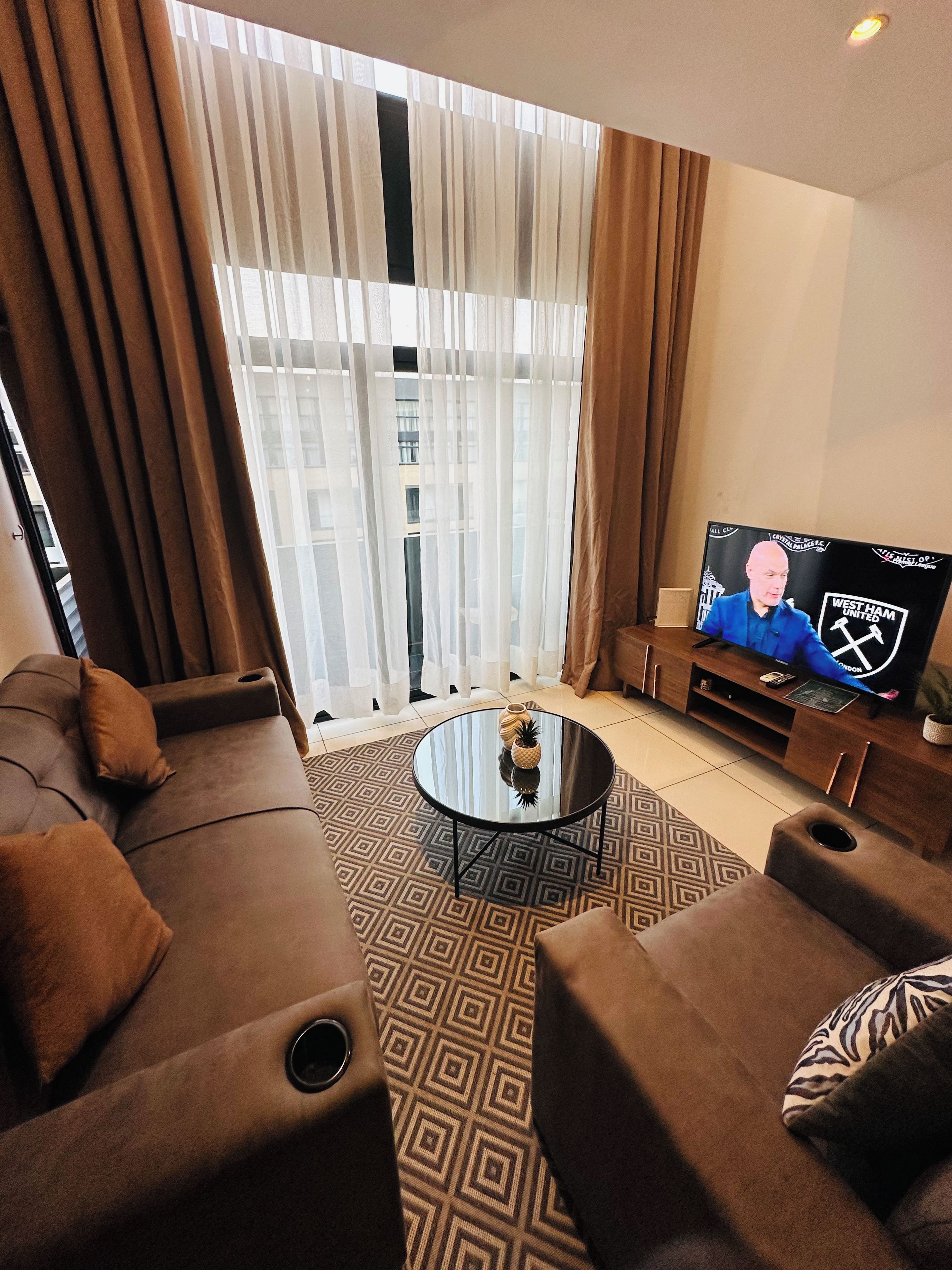 Una sala moderna con un sofá, una mesa de centro y un televisor mostrando un canal deportivo.